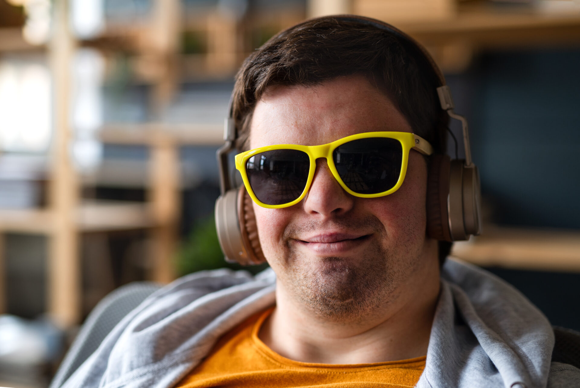 A close up of happy young man with Down syndrome with sunglasses and headset sitting indoors