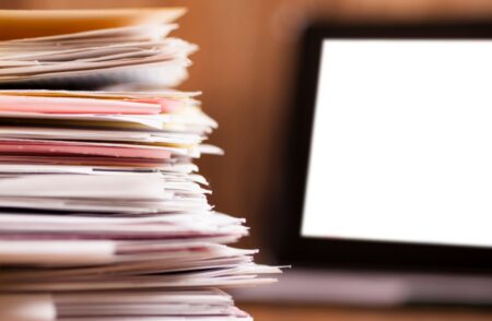 Stack of paperwork next to a computer screen